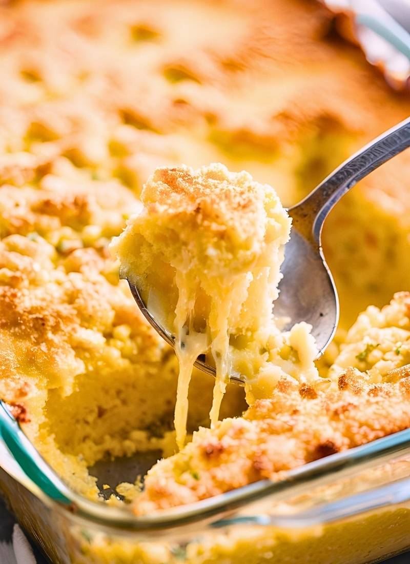 A close up of a spoon scooping cornbread casserole – revealing the moist, fluffy interior with a golden crust, perfectly capturing its comforting texture.