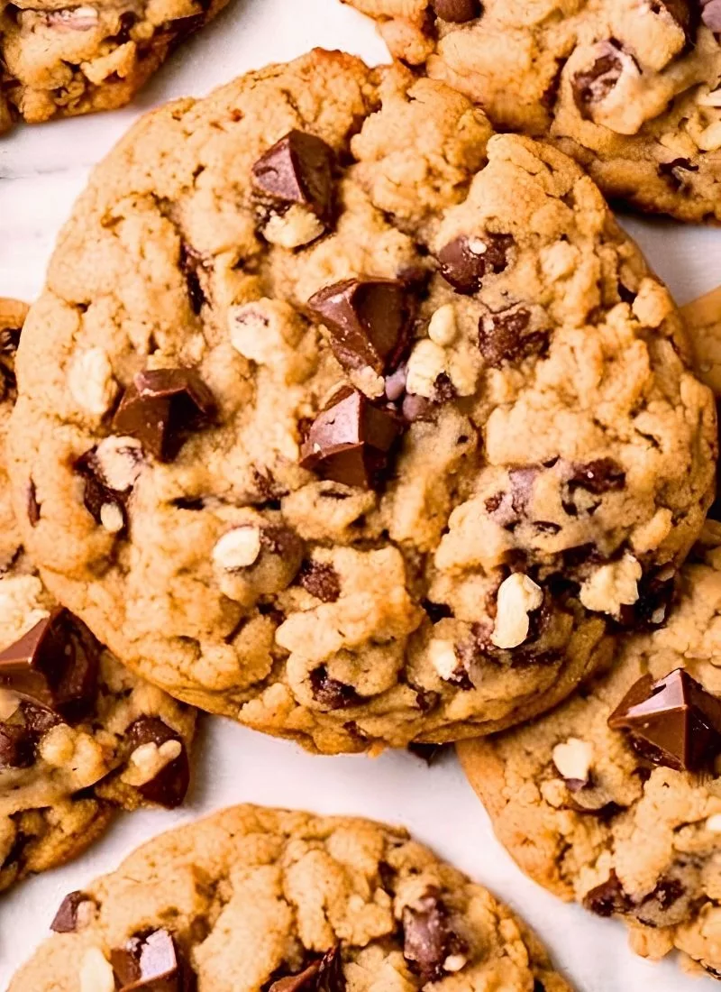 A close up shot of oatmeal chocolate chip cookies fresh from the oven, highlighting their golden brown edges, slightly cracked tops, and gooey melted chocolate chips. The oats add a rustic texture