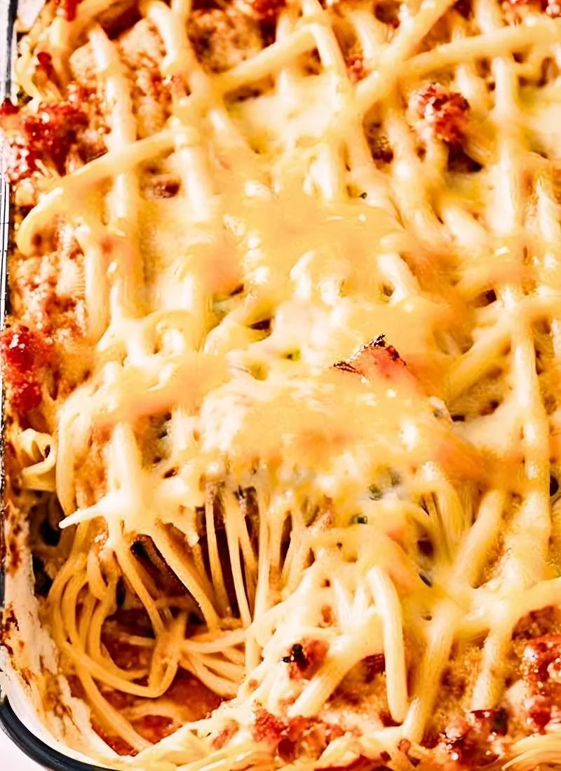 A fork lifting a cheesy bite from the Spaghetti Casserole Baked with strings of melted cheese stretching between the layers The rich red sauce clings to the spaghetti making it look hearty