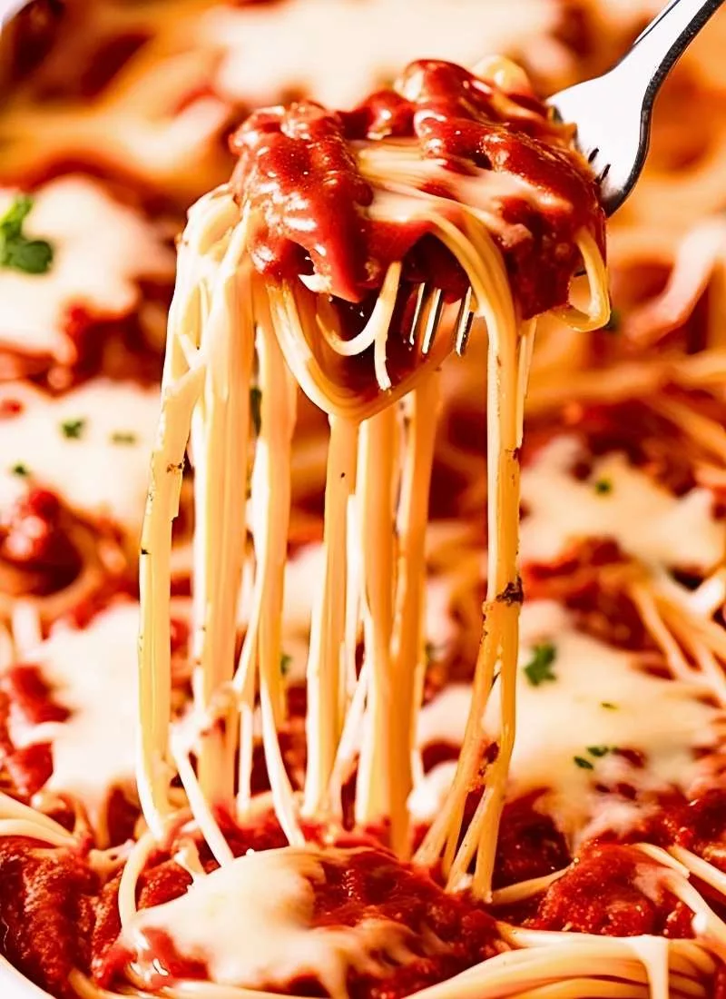 A fork lifting a cheesy bite from the Spaghetti Casserole Baked with strings of melted cheese stretching between the layers The rich red sauce clings to the spaghetti making it look hearty cre