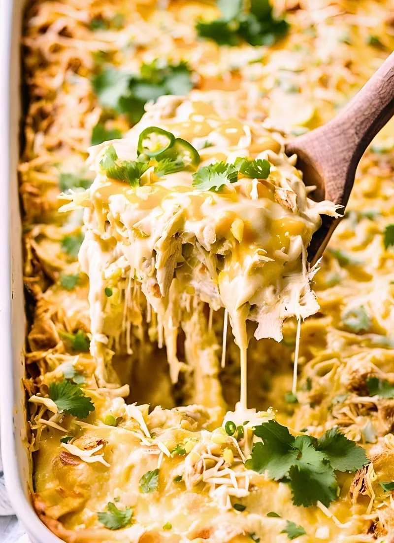 A heaping spoonful of Green Chili Chicken Enchilada Casserole being lifted from the baking dish, showcasing layers of creamy shredded chicken, melted cheese, and soft corn tortillas. The scoop dri