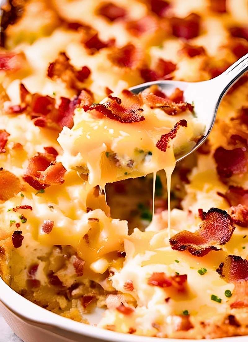 A spoon lifting a portion of loaded baked potato casserole revealing gooey melted cheese stretching from the creamy potatoes with bits of crispy bacon throughout Natural texture no overexpose