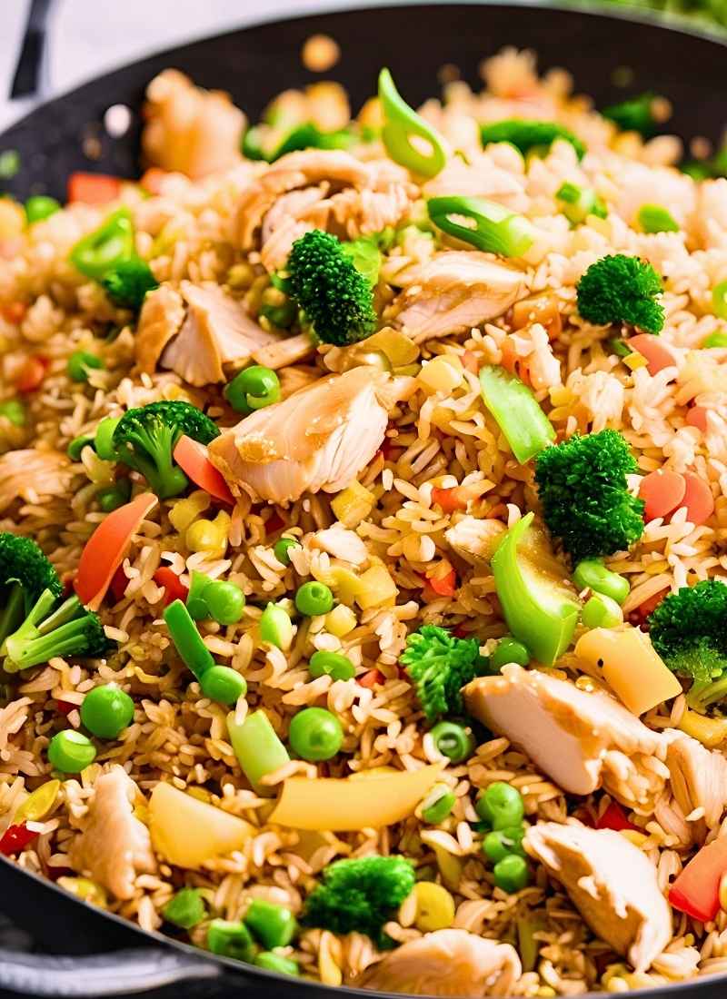 Close up of chicken fried rice in a wok – tender chicken pieces, fluffy golden rice, and vibrant veggies tossed together, capturing the glossy, freshly stir fried texture. (1)