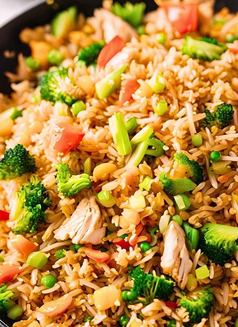 Close up of chicken fried rice in a wok – tender chicken pieces, fluffy golden rice, and vibrant veggies tossed together, capturing the glossy, freshly stir fried texture.