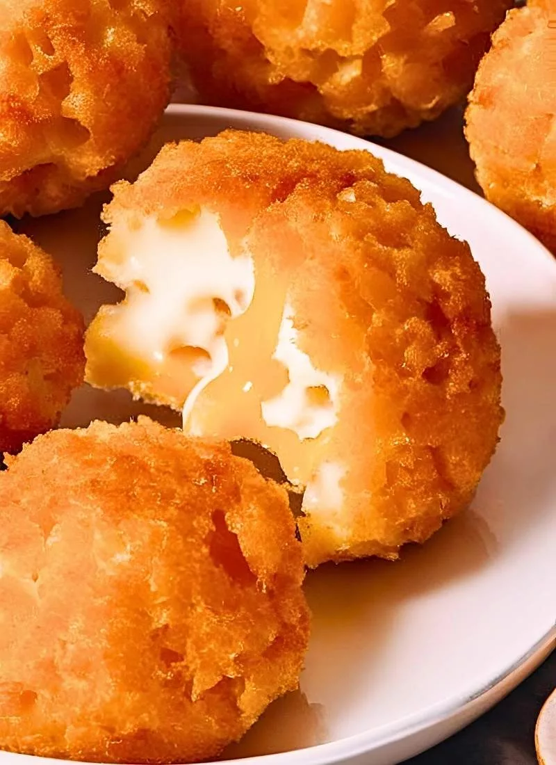 Close up of crispy golden brown Cheese Balls stacked on a plate – The perfectly round crunchy exterior glistens lightly with a few cracked open revealing gooey melted cheese inside ()