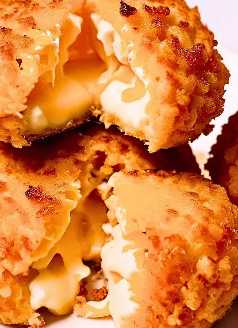 Close up of crispy golden brown Cheese Balls stacked on a plate – The perfectly round crunchy exterior glistens lightly with a few cracked open revealing gooey melted cheese inside