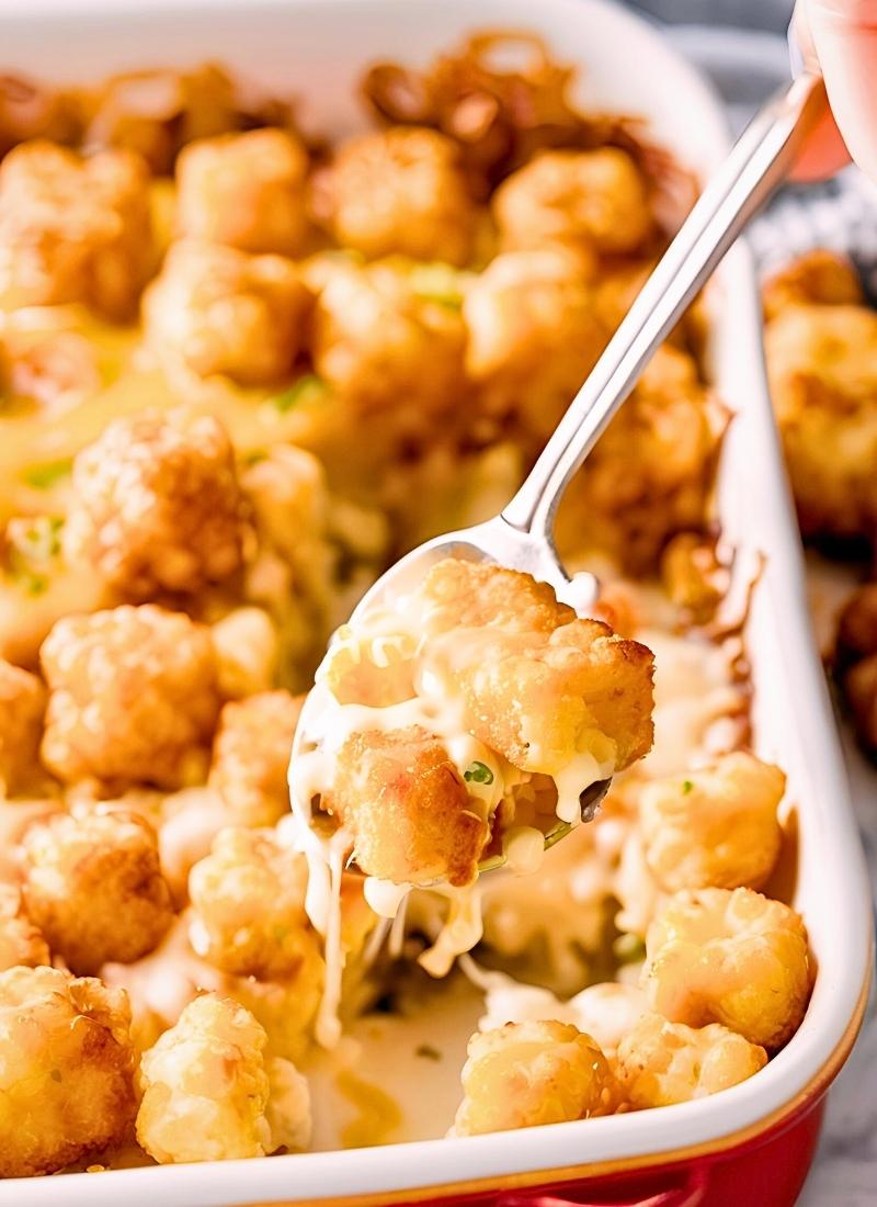 Spoon scooping a serving of tater tot casserole – a natural close up of a spoon lifting a portion, revealing gooey melted cheese, creamy filling, and crispy tater tots.